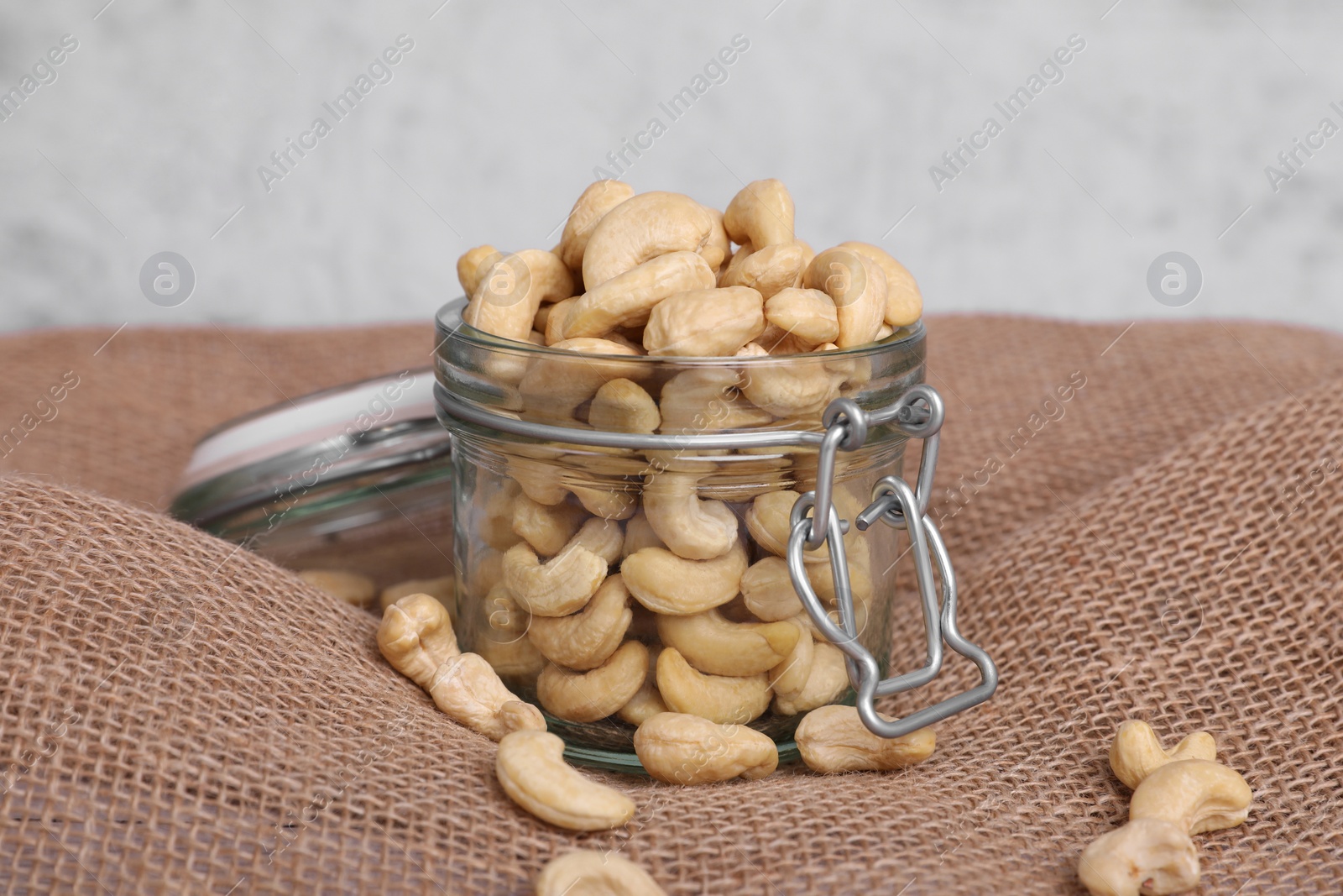 Photo of Tasty cashew nuts in glass jar on light brown fabric, closeup