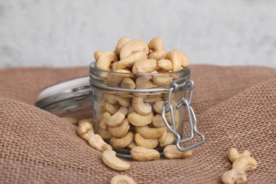 Tasty cashew nuts in glass jar on light brown fabric, closeup