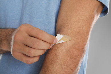 Photo of Man putting sticking plaster onto arm against light grey background, closeup