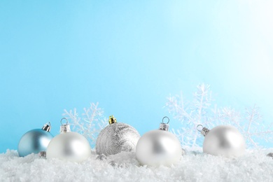 Photo of Christmas tree decoration on artificial snow against light blue background. Space for text