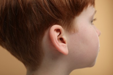 Hearing problem. Little boy on pale brown background, closeup