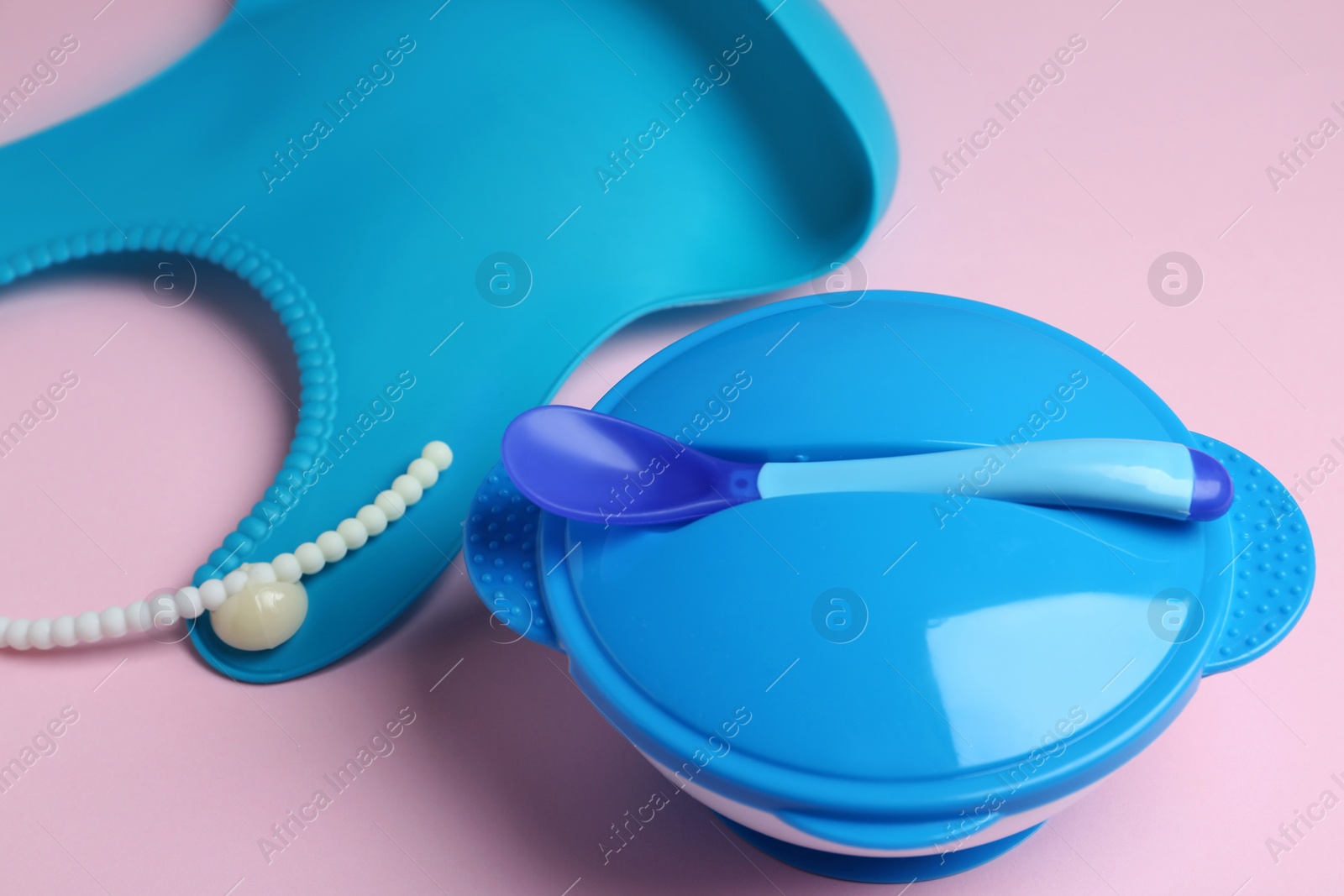 Photo of Plastic dishware and silicone bib on light pink background. Serving baby food