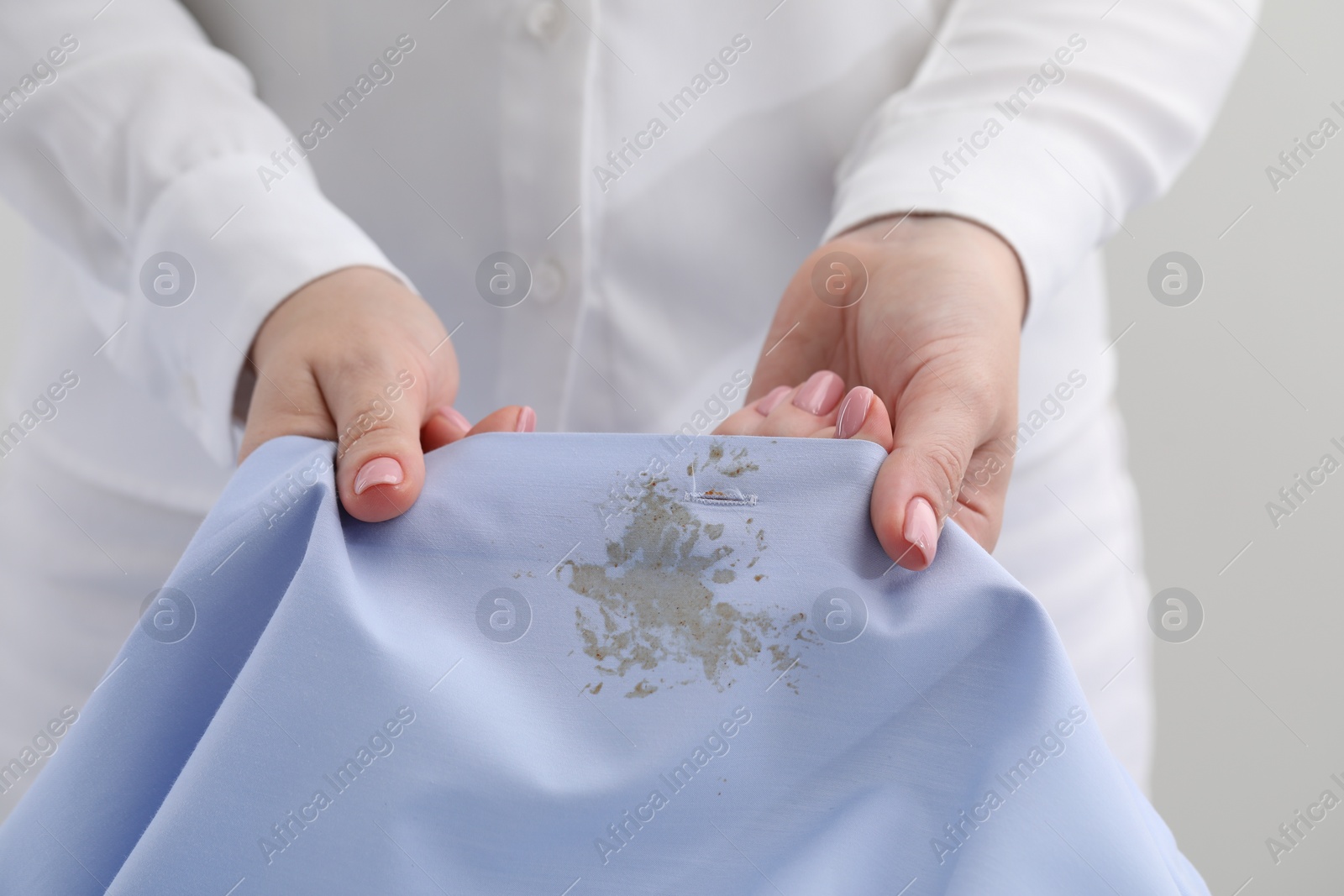 Photo of Woman holding shirt with stain against light background, closeup