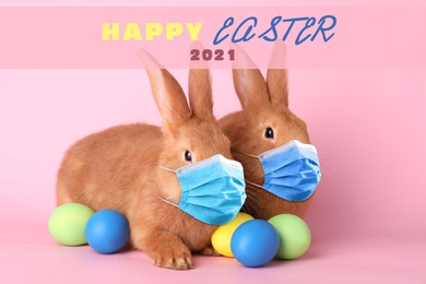 Text Happy Easter 2021 and cute bunnies in protective masks on pink background. Holiday during Covid-19 pandemic