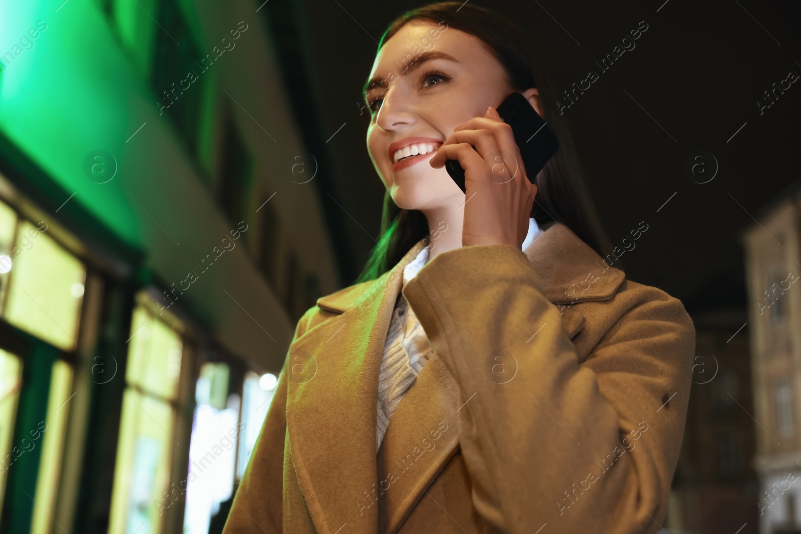 Photo of Smiling woman talking by smartphone on night city street