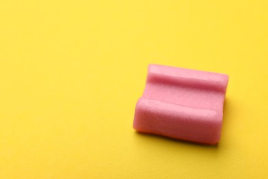 Photo of Tasty pink chewing gum on yellow background, closeup. Space for text