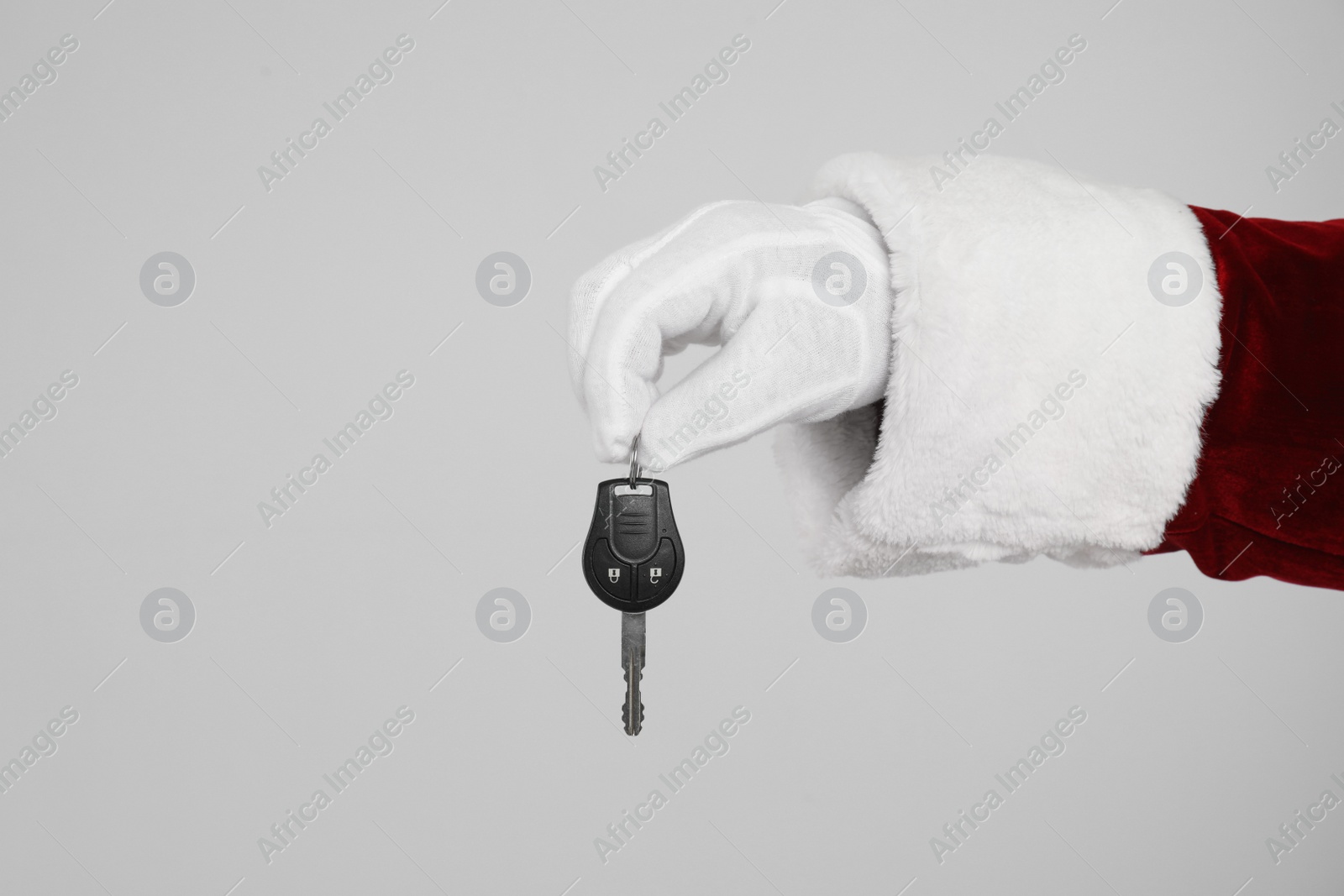 Photo of Santa Claus holding car key on light grey background, closeup of hand