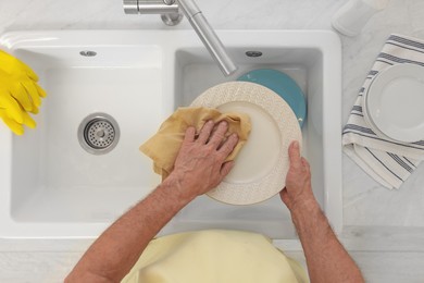 Man wiping plate above sink, top view