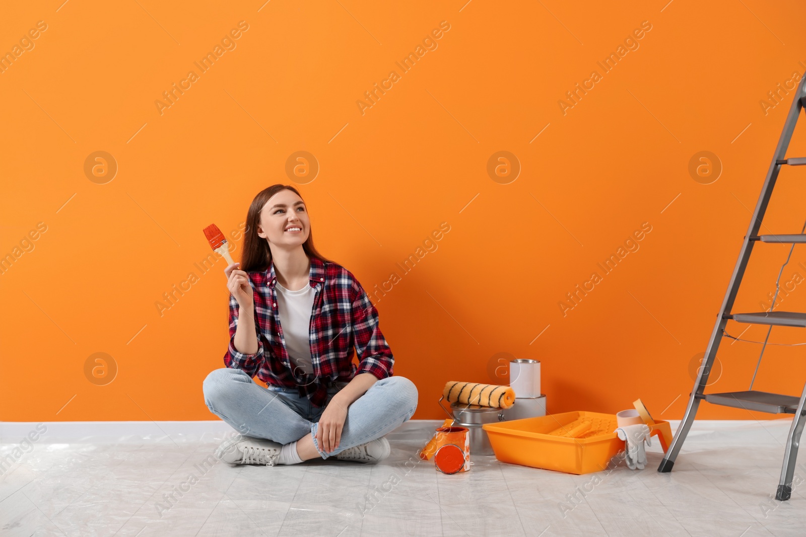 Photo of Happy designer with brush and painting equipment near freshly painted orange wall indoors