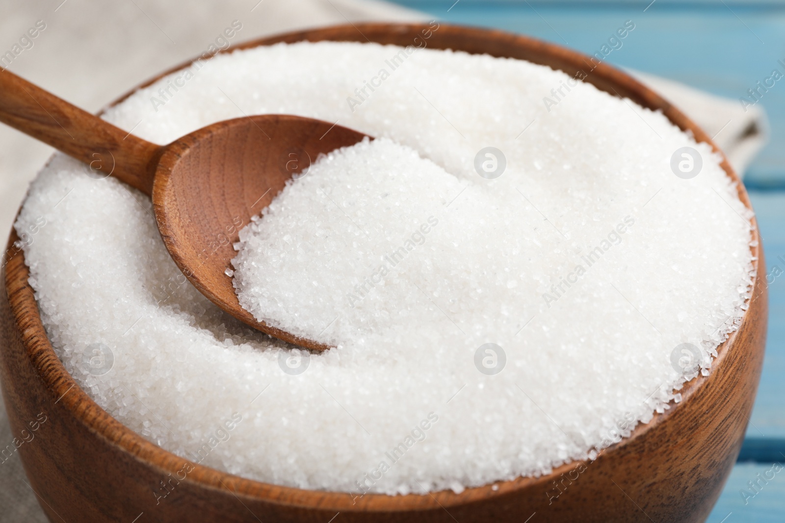 Photo of Granulated sugar and spoon in bowl on table, closeup