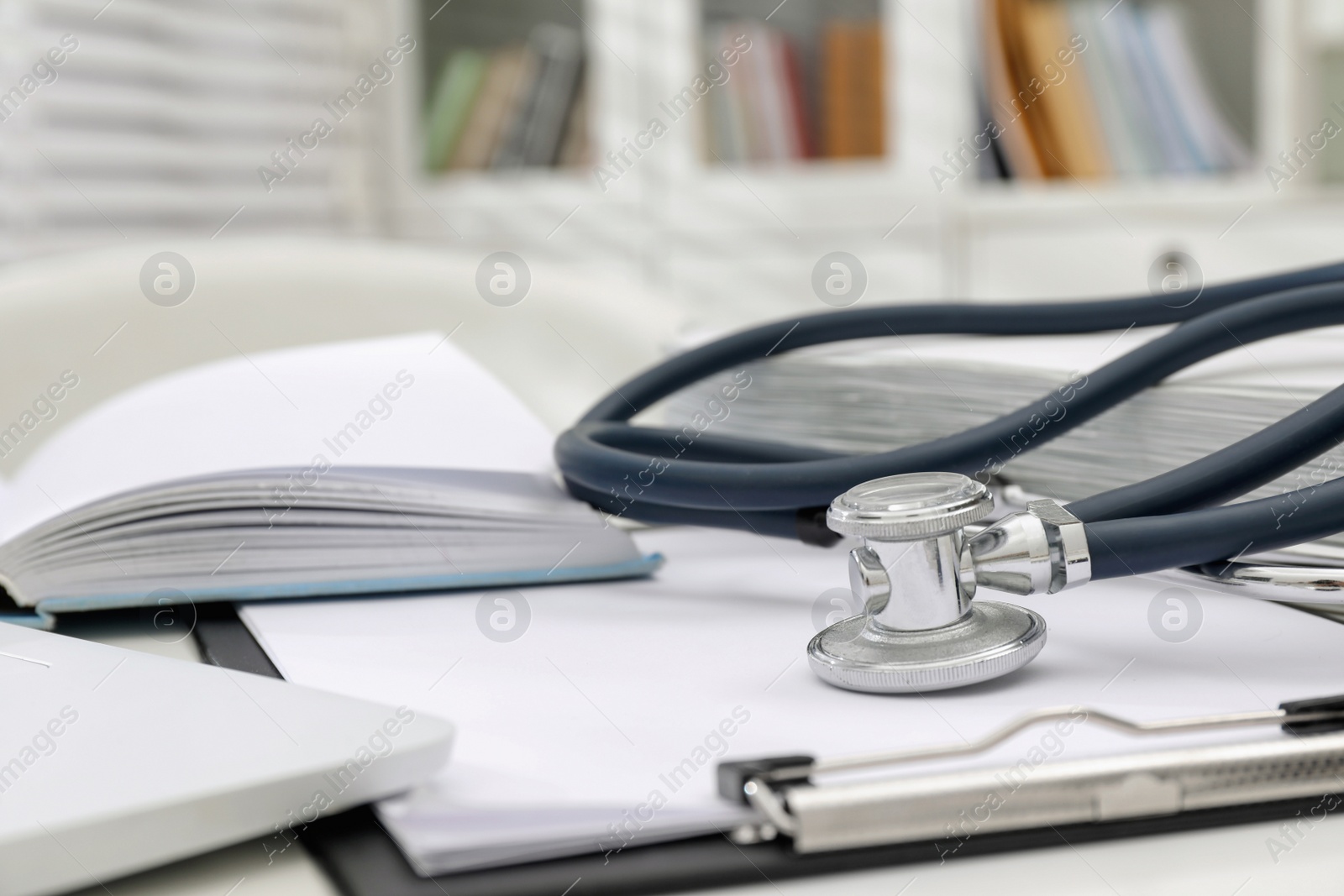 Photo of Book, stethoscope and clipboard on white table indoors, closeup with space for text. Medical education