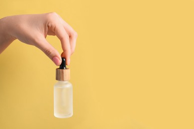 Woman holding bottle with serum against pale orange background, closeup. Space for text