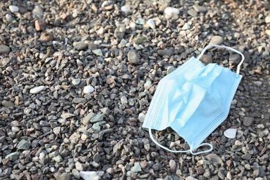 Photo of Used disposable face mask on small pebbles outdoors. Space for text