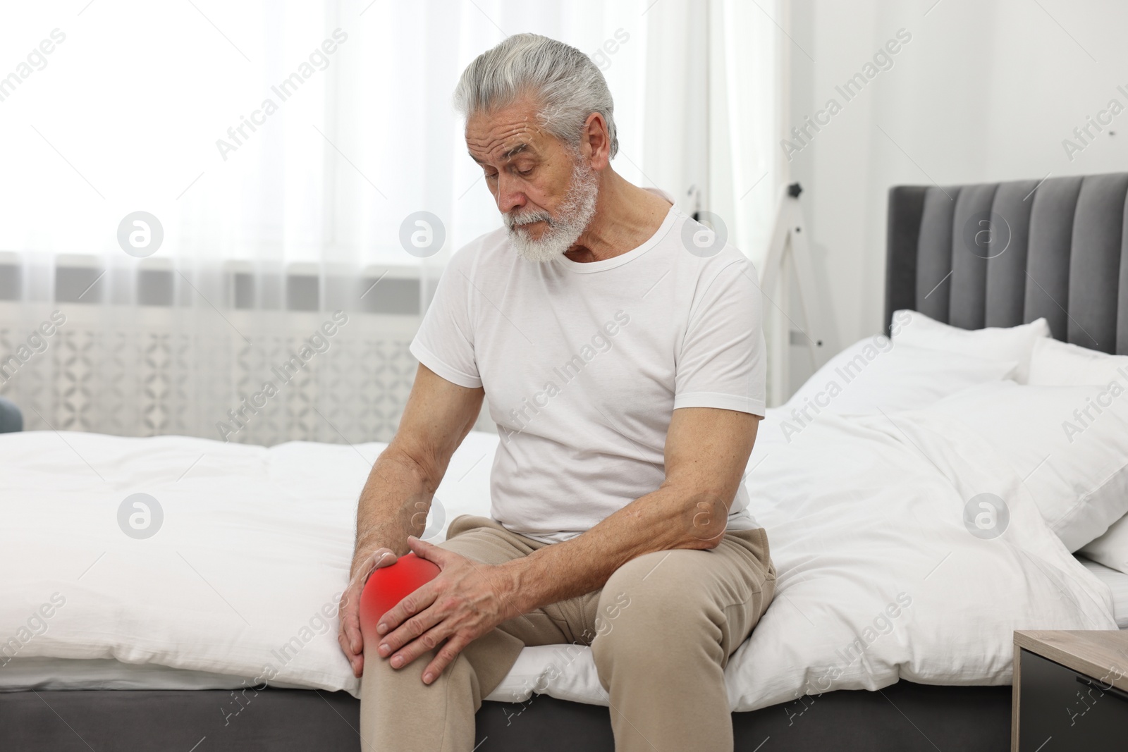 Image of Senior man suffering from pain in knee on bed at home