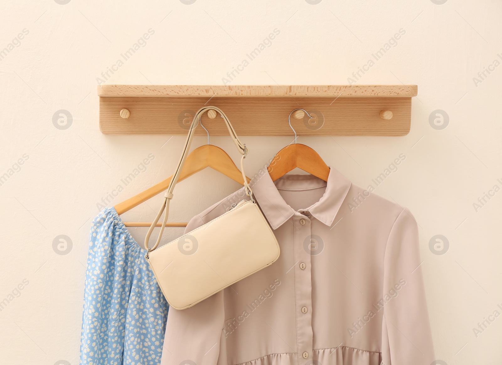 Photo of Wooden shelf with fashionable clothes and bag on beige wall. Interior element