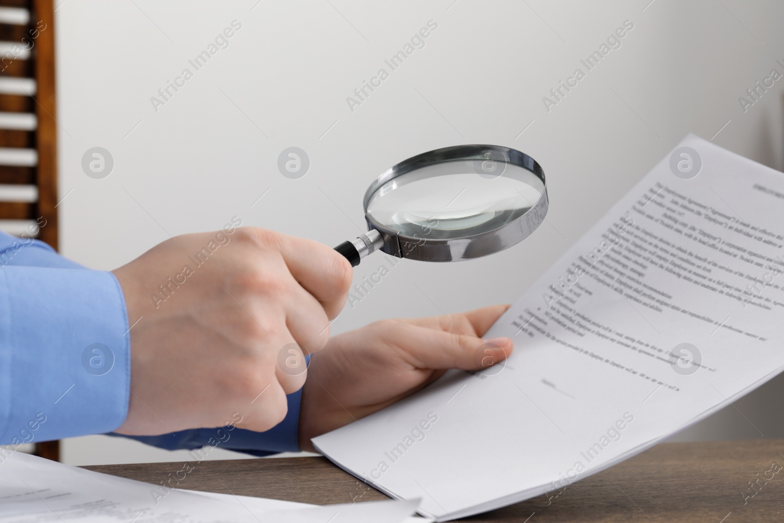 Photo of Man looking at document through magnifier at wooden table, closeup. Searching concept