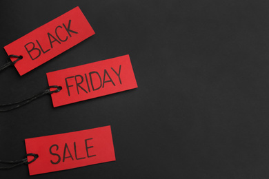 Red tags with words BLACK FRIDAY SALE on dark background, flat lay. Space for text