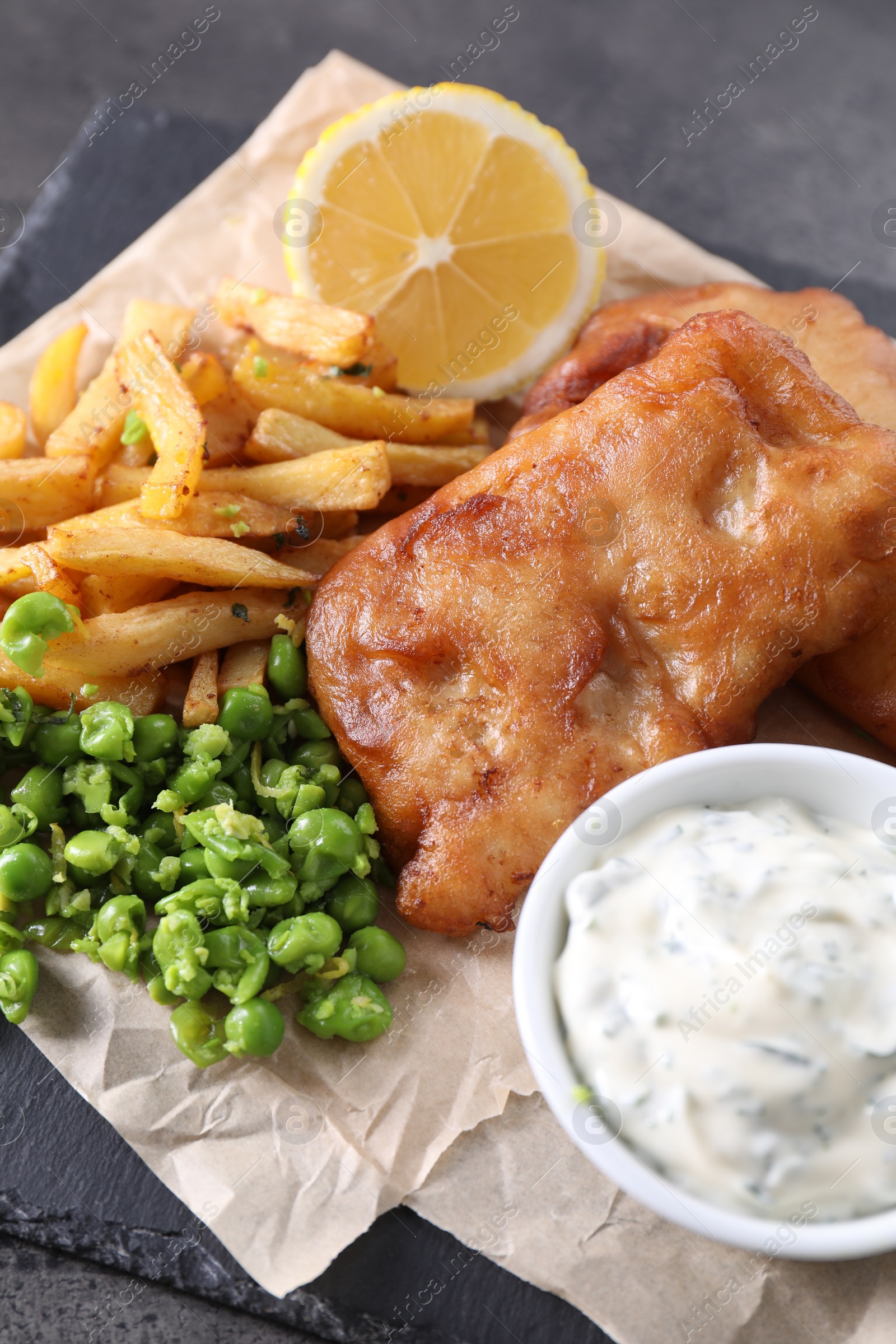 Photo of Tasty fish, chips, sauce and peas on grey table, closeup