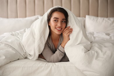 Photo of Beautiful young woman wrapped with soft blanket relaxing in bed at home