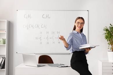 Photo of Young chemistry teacher giving lesson near whiteboard in classroom. Space for text