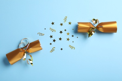 Photo of Open golden Christmas cracker with shiny confetti on light blue background, top view