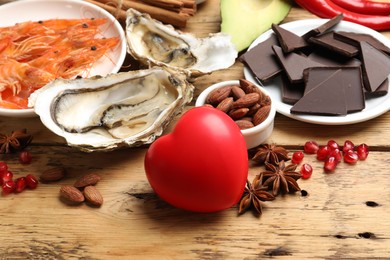 Photo of Natural aphrodisiac. Different food products and heart model on wooden table, closeup