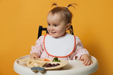 Photo of Cute little baby wearing bib while eating on yellow background