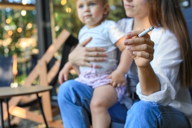 Mother with cigarette and child outdoors, focus on hand. Don't smoke near kids