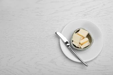 Photo of Bowl with tasty fresh butter and knife on wooden table, top view