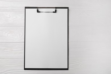 Photo of New clipboard with sheet of blank paper on white wooden table, top view. Space for text