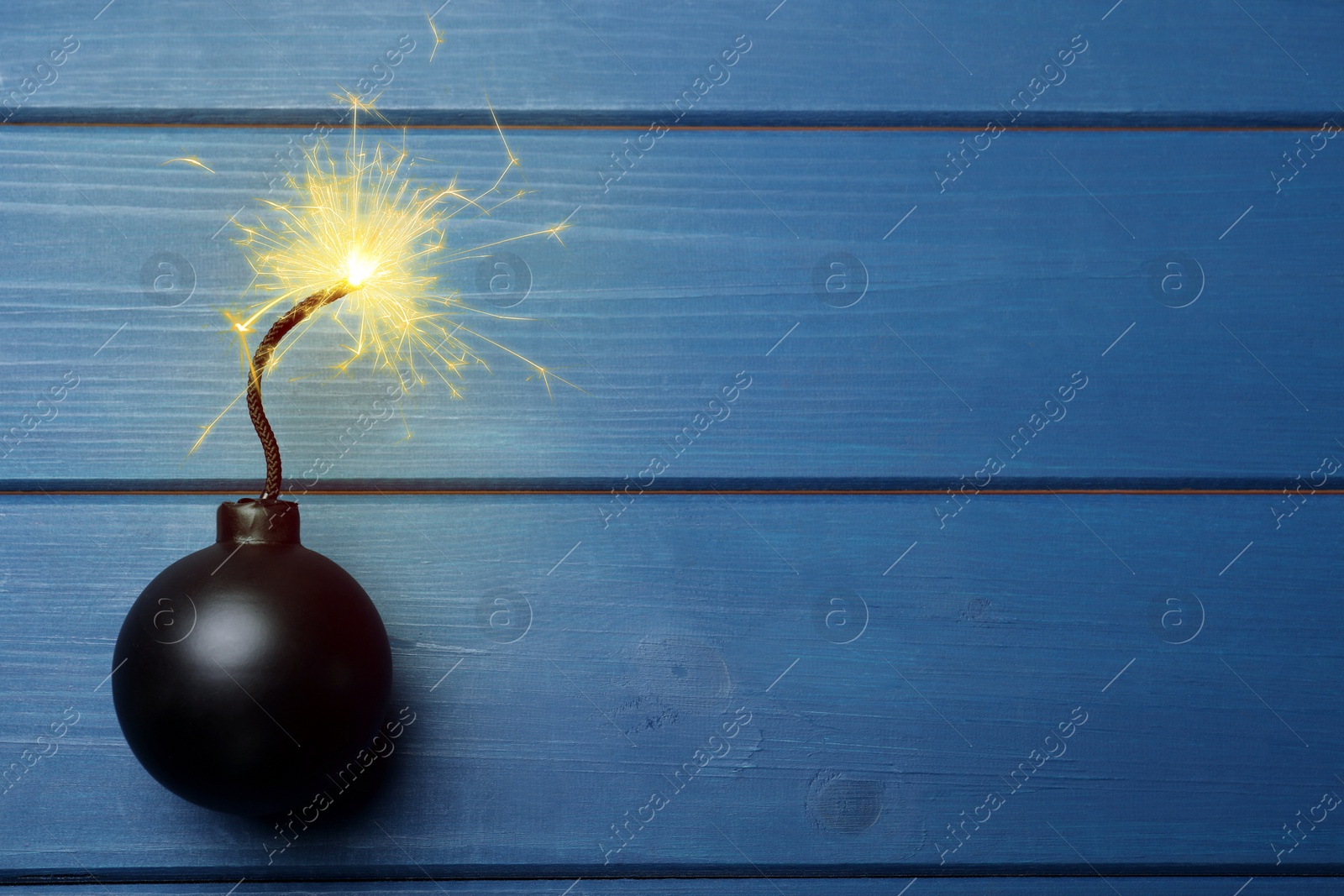 Image of Old fashioned black bomb with lit fuse on blue wooden table, top view. Space for text