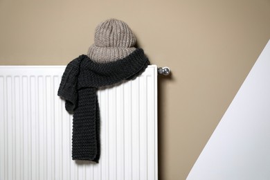 Modern radiator with knitted hat and scarf near color wall indoors, space for text