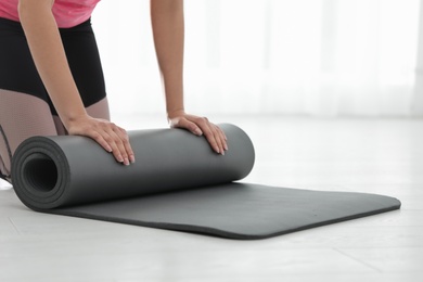 Young woman rolling yoga mat indoors, closeup. Space for text