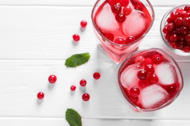 Tasty cranberry juice with ice cubes in glasses and fresh berries on white wooden table, flat lay. Space for text