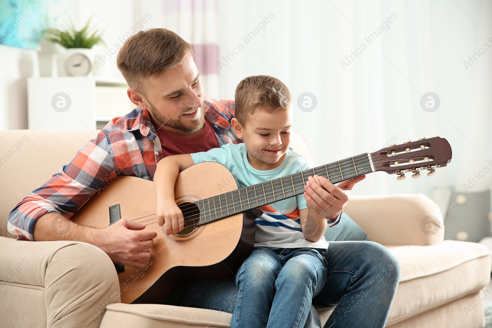 Photo of Father teaching his little son to play guitar at home