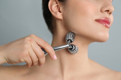 Photo of Woman using metal face roller on grey background, closeup