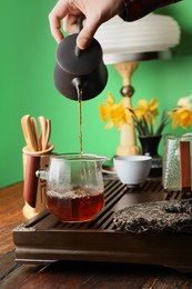 Woman pouring freshly brewed pu-erh tea into pitcher at wooden table, closeup