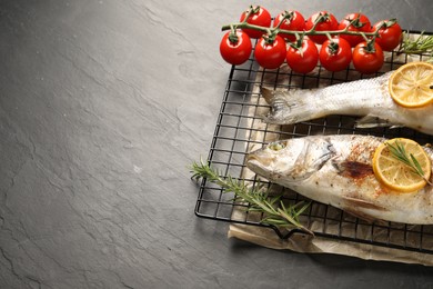 Baked fish with tomatoes, rosemary and lemon on black textured table, space for text