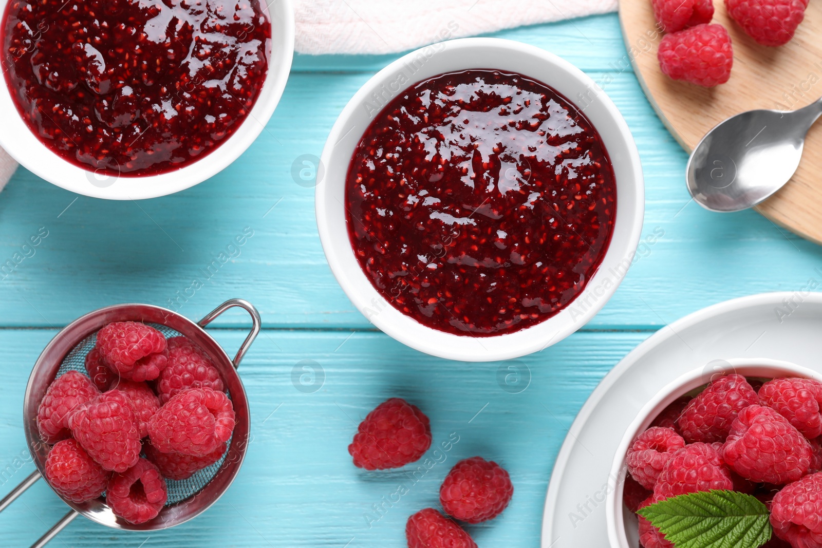 Photo of Delicious jam and fresh raspberries on blue wooden table, flat lay
