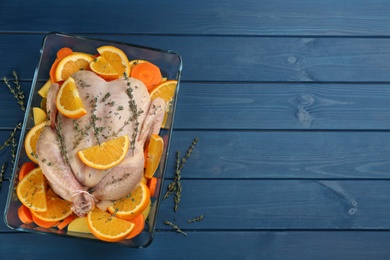 Photo of Raw chicken with orange slices, potatoes and thyme on blue wooden table, flat lay. Space for text
