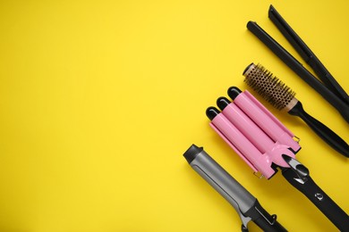 Photo of Different curling irons, hair straightener and round brush on yellow background, flat lay. Space for text