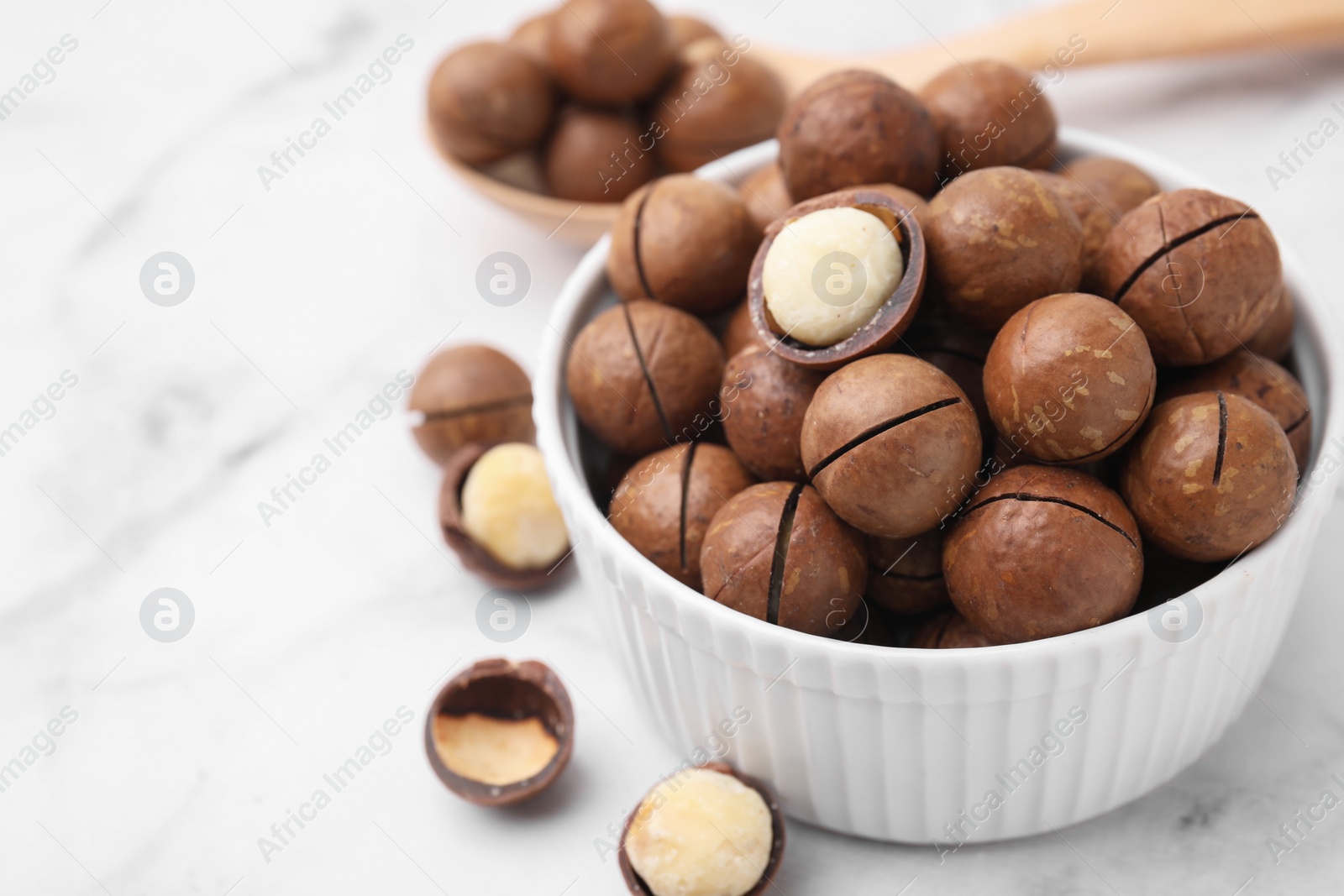 Photo of Tasty Macadamia nuts in bowl on white marble table, closeup. Space for text