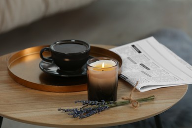 Photo of Beautiful candle, lavender, newspaper and cup of coffee on round wooden table indoors