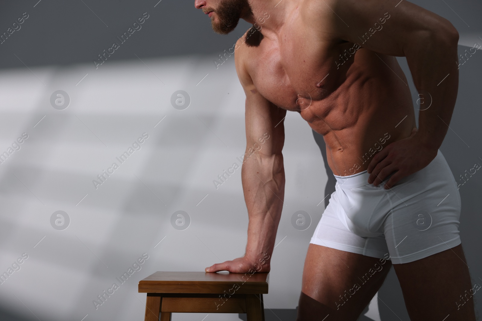 Photo of Young man in stylish white underwear near grey wall, closeup. Space for text