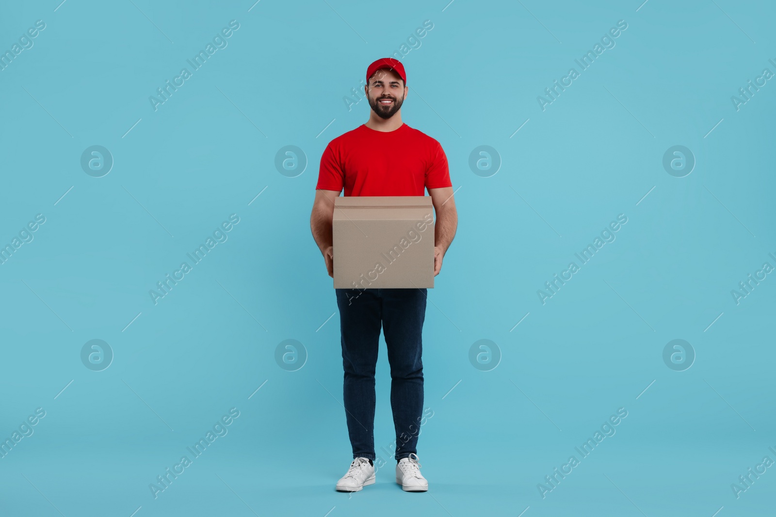Photo of Happy young courier with parcel on light blue background