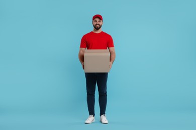 Happy young courier with parcel on light blue background