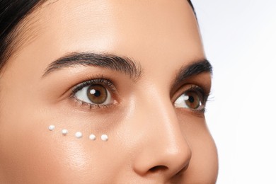 Photo of Closeup view of young woman with cream on skin under eye against white background