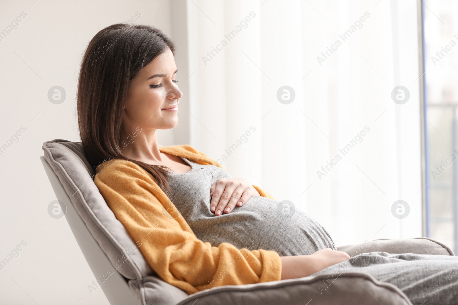 Photo of Young pregnant woman resting in armchair at home