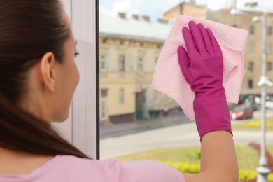 Photo of Young woman cleaning window glass with rag at home, closeup
