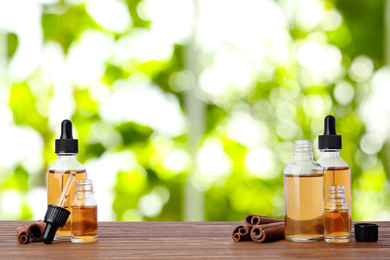 Bottles of essential oil and cinnamon sticks on wooden table against blurred background. Space for text